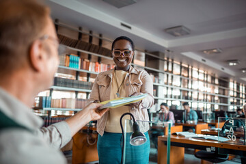 Young female student taking a book from a librarian in the high school library