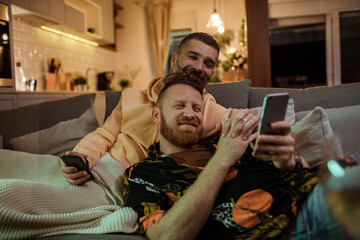 Gay couple sharing a tender moment while taking a selfie on the couch