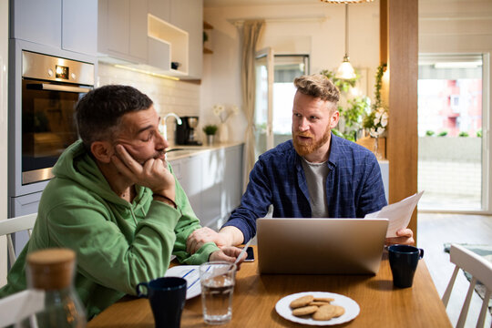 Gay couple discussing paperwork over coffee in their kitchen