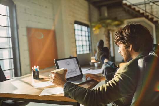 Relaxed businessman sipping coffee while working in a sunlit loft