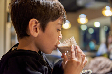 close-up portrait of latino little boy in profile in a bar drinking hot chocolate milk. Out of...