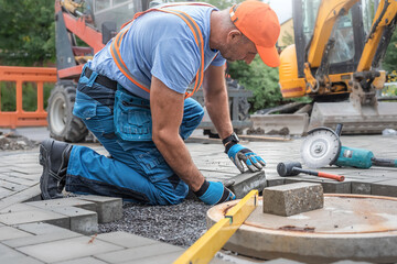 Laying interlocking paving. A worker's hand is placing interlocking paving stones around the sewer...