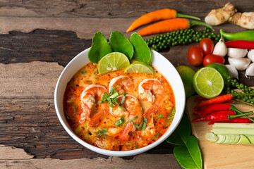Tom Yum Goong or Shrimp soup spicy sour Soup Traditional food in Thailand contains chili, lime,lemongrass, lime leaf, along with cooked rice in a white dish on the old wood background. - obrazy, fototapety, plakaty