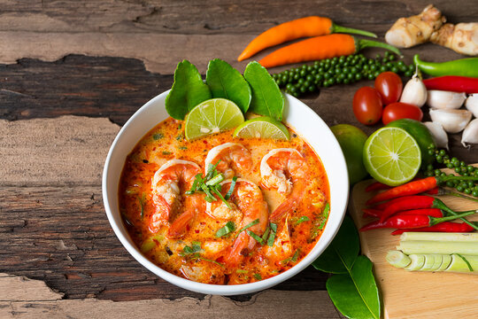 Tom Yum Goong or Shrimp soup spicy sour Soup Traditional food in Thailand contains chili, lime,lemongrass, lime leaf, along with cooked rice in a white dish on the old wood background.