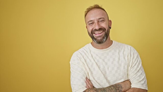 Attractive young man, standing with a confident smile and casual arms crossed gesture. isolated on a yellow background, exuding sheer happiness and positive joy.
