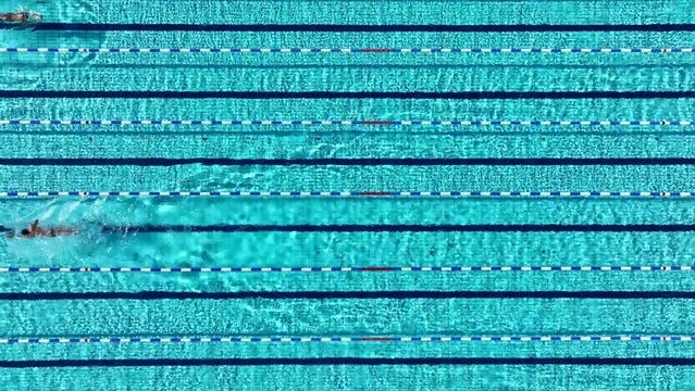 Aerial drone top down video of athletes practice in turquoise swimming pool made for competition