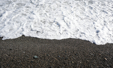 pebble stones by the sea. Silky waves of blue water. Black sea. Pebble rimmed beach. Sea sunset waves with foam. Waves run on pebbles and rocks. Water breaks into splashes and foam.  aerial top view.