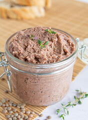 Close up of Vegan spread made with lentils and nuts on a rustic bread slice and in a glass jar, decorated with rosemary. Vegan dipping.