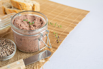 Vegan spread made with lentils and nuts on a rustic bread slice and in a glass jar, decorated with rosemary. Copy space on right side. Vegan dipping.