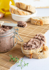Vegan spread made with lentils and nuts on a rustic bread slice and in a glass jar, decorated with rosemary. Vegan dipping.