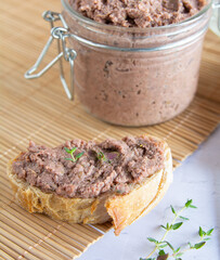 Vegan spread made with lentils and nuts on a rustic bread slice and in a glass jar, decorated with rosemary. Vegan dipping.