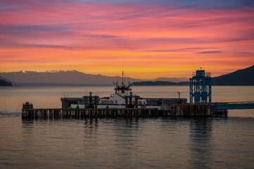 Fototapeta premium Ferry boat docking at an island in the Salish Sea during a dramatic sunrise. The Whatcom Chief services Lummi Island commuters traveling to the mainland. Washington, USA
