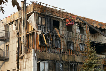 A building destroyed by fire in copati and black soot. A repair team in a construction cradle...