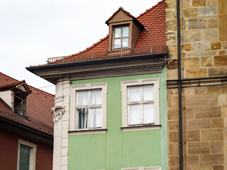 Narrow building next to a sandstone wall. Close up of the house exterior with the windows. The architecture is old and is part of the historical town center. On the rooftop is a gabled dormer.