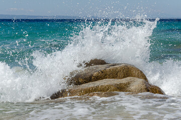 frothy wave crashes against  coastal rock