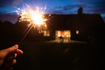 Hand holding a sparkler, or bengal fire stick, burning in outdoor setting at blue hour dusk with a...