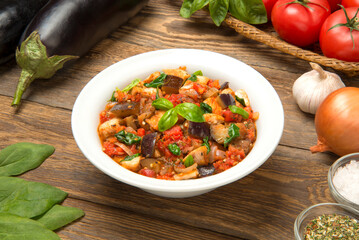Eggplant stew with tomatoes and spinach in a salad bowl on a rustic table with
ingredients.
- 671792146