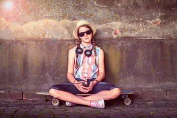Portrait of a teenage girl sitting on a skateboard leaning against a wall in the city