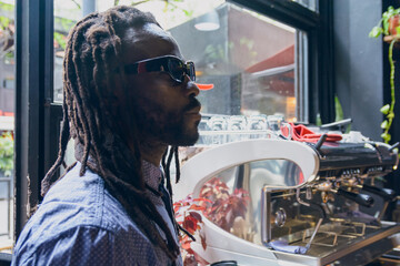 young african man with dreadlocks standing at restaurant counter watching and thinking what to order