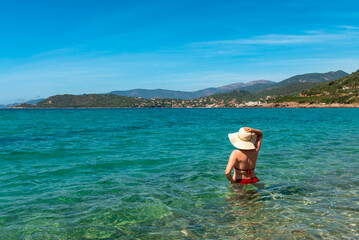 Fototapeta na wymiar A woman in a hat immersed in the beautiful sea, Corsica, France