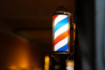Barber pole of barbershop in the evening. Classic barbershop spinning cylinder to attract customers. Background with copy space. - obrazy, fototapety, plakaty