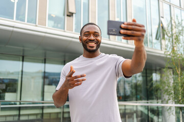 African American man holding smartphone having video chat on urban street in city. Guy blogger chatting with best friends in social network. Man having virtual meeting online chat video call outdoor