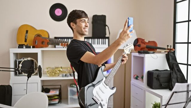 Handsome young hispanic man jazzing up the music studio, talking and jamming on his electric guitar during a vibrant video call