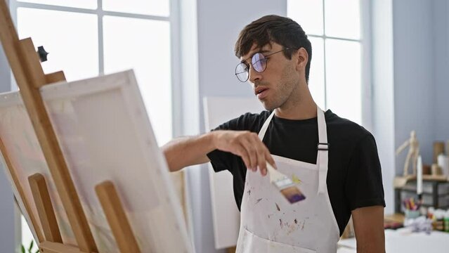 Young, confident hispanic man joyfully sweating as he lets creativity flow, artist diligently drawing on canvas in vibrant studio