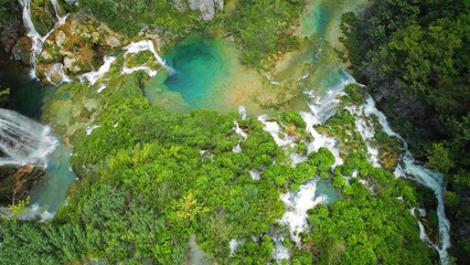 Plitvice waterfalls in mountain landscape of Croatia. Blue and green can be seen in the cascades. Water streams flow into a lake.