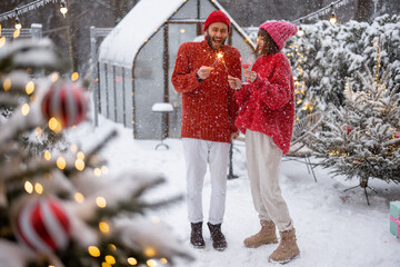 Man and woman in red sweaters celebrate New Year's holidays by lighting sparklers and having fun...