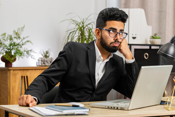 Tired Indian businessman feeling worried about financial problem, stress at home office workplace. Indian freelancer broker man frustrated thinking of money debt, budget loss, bankruptcy. Overworking