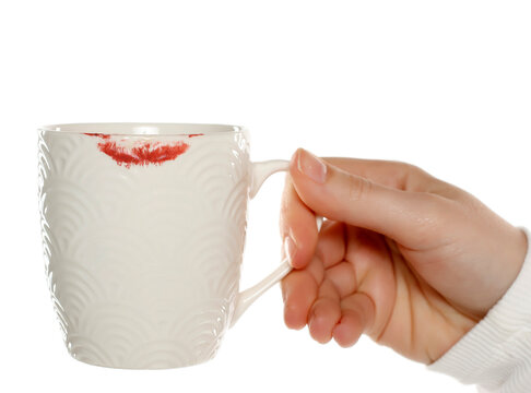 Woman's hand hold a c eramic cup with lipstick mark on white background