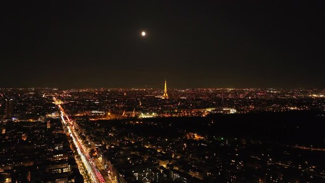 Aerial panoramic view of large city. Illuminated popular Eiffel Tower with rotating spotlight on top. Paris, France