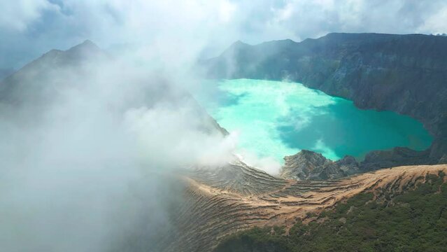 Active volcano Kawah Ijen in the crater with sulfur lake turquoise color and smoke emissions from burning sulfur, East Java, Indonesia. Aerial Drone view 4K.