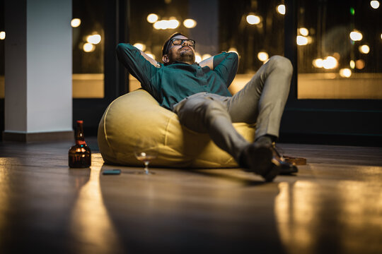 Young businessman sitting in bag chair and drinking cognac after successfull day on work