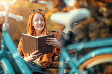 Woman read a book in autumn park - obrazy, fototapety, plakaty