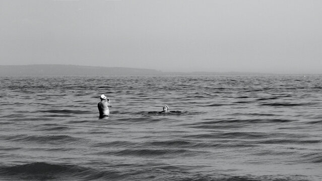 monochrome image of man taking photo of woman in the sea.