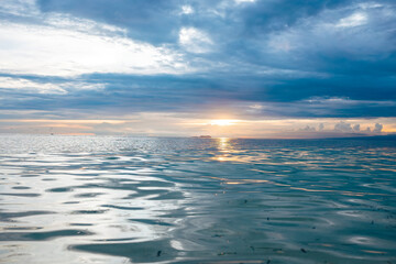 The sun's last rays pierce the horizon, casting a dance of colors upon the rippling ocean beneath a...