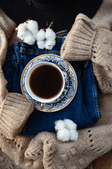 Winter outfit layout. Flat lay of beige knitted sweater, blue jeans, cotton flower and tea in a cup on rustic wooden background, top view. Winter clothes and mood