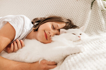 Close-up of a teenage girl lying on the sofa and hugging her favorite white fluffy cat. Children and animals. - obrazy, fototapety, plakaty