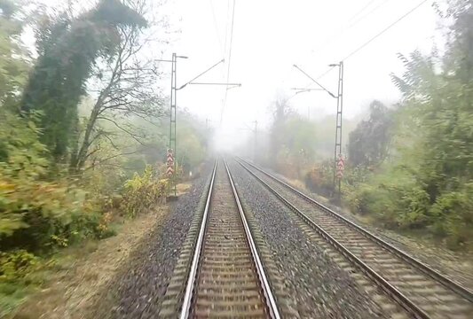 Front view or driver cabin view of a train travelling on tracks in the city with autumn trees during fall