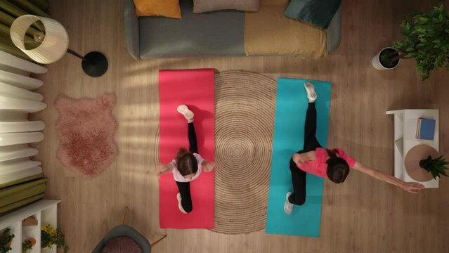 In the shot above, a woman and a child, they are standing on fitness mats in a room in sports uniforms and doing a sports exercise, stretching. Doing yoga. Then they finish and sit on their knees
