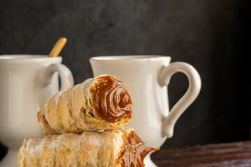 Composition of Argentine snack with cannon of dulce de leche and cup with infusion.