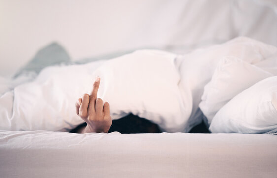 Angry, hand and person with insomnia in bed with a middle finger for morning or waking up, sleeping in bedroom and at home. Hand, show a curse sign and frustrated with sleep problem at night