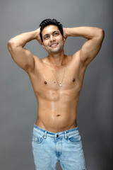 Fototapeta premium Portrait of a shirtless young man. Healthy muscular man with black hair, posing with hands behind head on grey background.