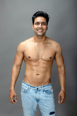 Fototapeta premium Portrait of a shirtless young man. Healthy muscular man with black hair, posing with hands behind head on grey background.