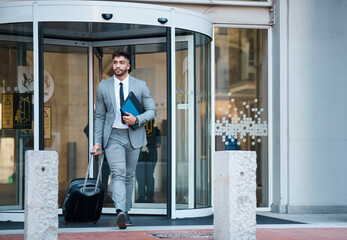 Businessman outside office, suitcase and travel for lawyer at law firm for work commute. Folder,...