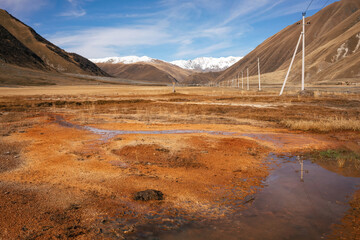 Rust-colored wetlands in the foreground of a vast mountainous expanse. Power lines trace a path across the untouched terrain