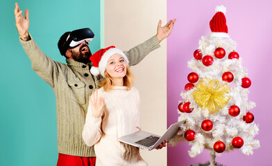 Happy family near Christmas tree. Bearded man in VR glasses and smiling woman in Santa hat with laptop show sign ok. 3d technology. Christmas couple. Winter holiday. Christmas or New Year celebration.