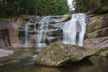 Mumlava waterfall, in the foreground granite stone. Mountain river Mumlava, Krkonose national park, Czech Republic, summer afternoon.